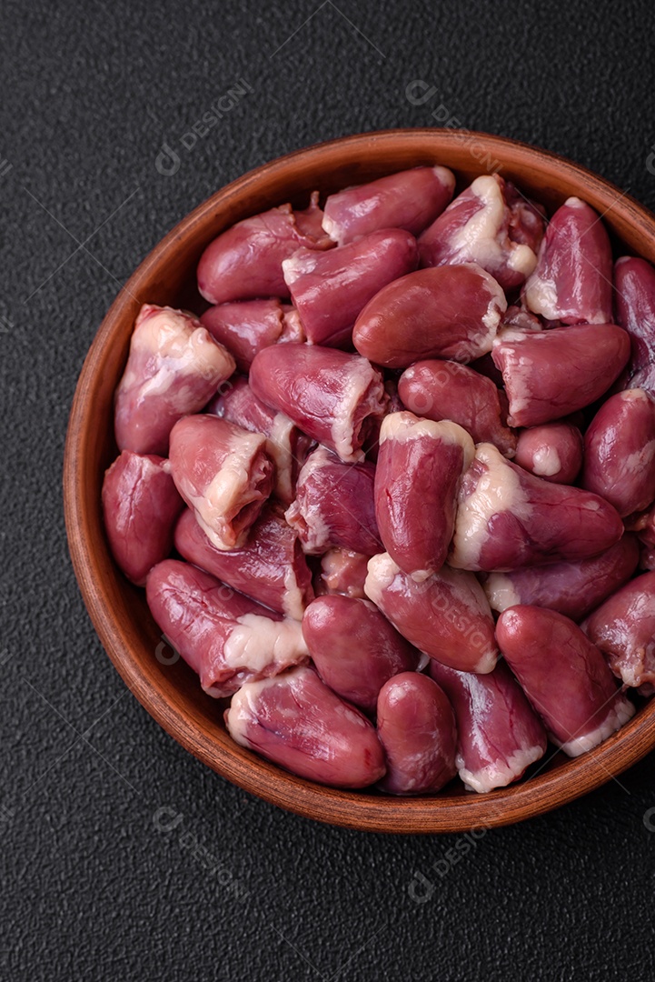 Corações frescos de frango cru, peru ou pato em uma placa de cerâmica com sal e especiarias sobre um fundo escuro de concreto