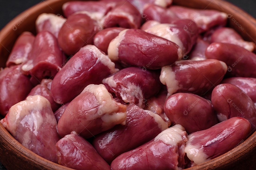 Corações frescos de frango cru, peru ou pato em uma placa de cerâmica com sal e especiarias sobre um fundo escuro de concreto