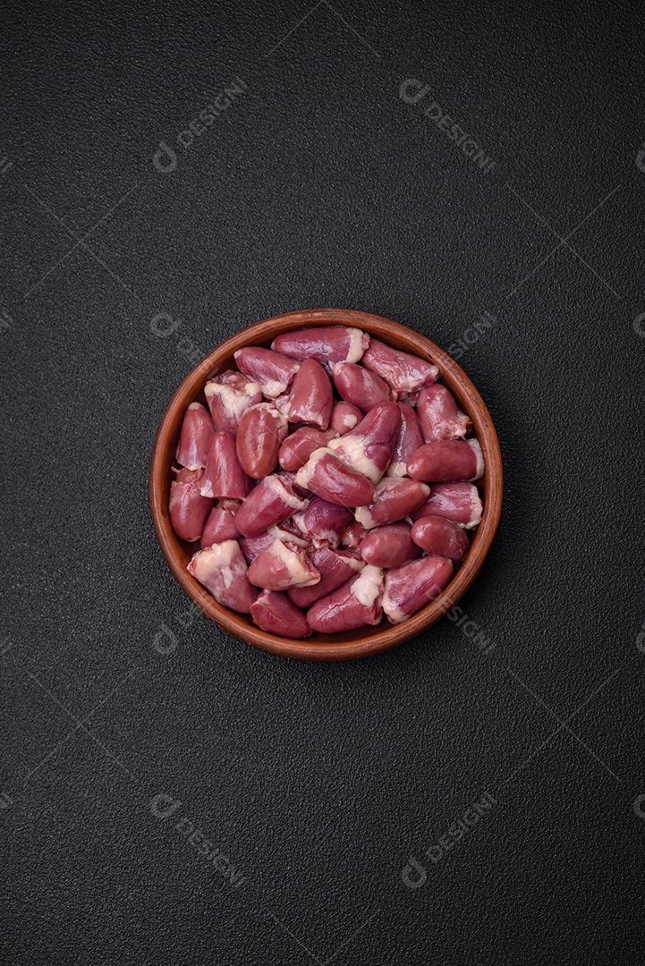 Corações frescos de frango cru, peru ou pato em uma placa de cerâmica com sal e especiarias sobre um fundo escuro de concreto