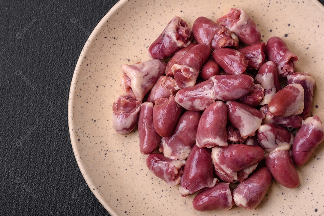 Corações frescos de frango cru, peru ou pato em uma placa de cerâmica com sal e especiarias sobre um fundo escuro de concreto