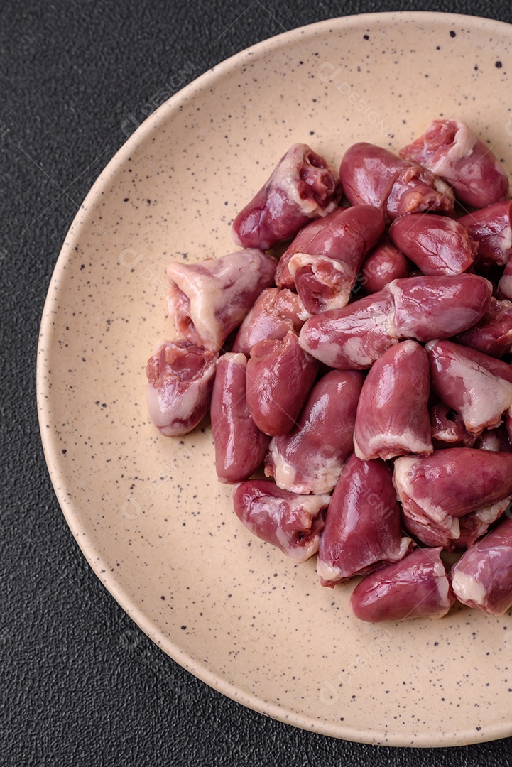 Corações frescos de frango cru, peru ou pato em uma placa de cerâmica com sal e especiarias sobre um fundo escuro de concreto