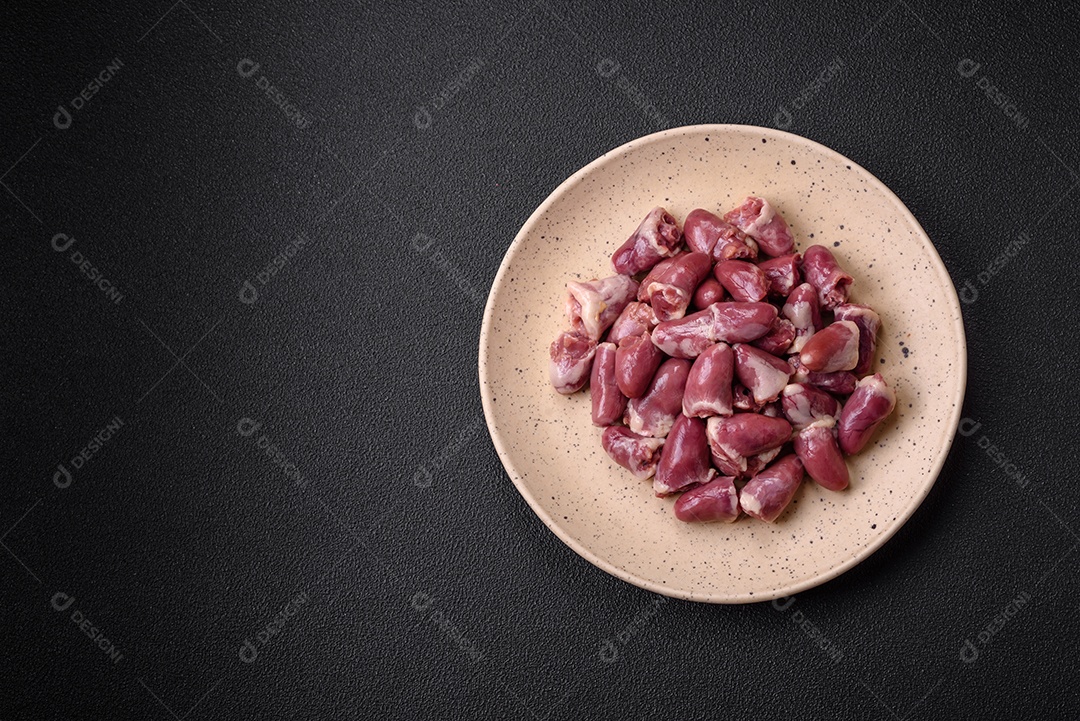 Corações frescos de frango cru, peru ou pato em uma placa de cerâmica com sal e especiarias sobre um fundo escuro de concreto