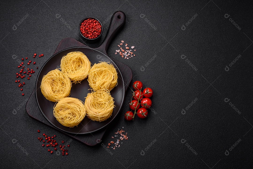 Massa crua de capellini ou macarrão com sal e especiarias sobre um fundo escuro de concreto