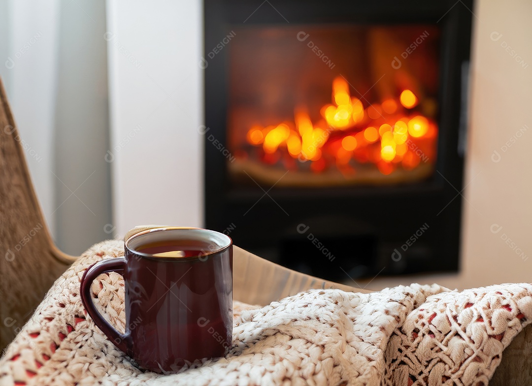 Uma caneca de chá quente está sobre uma cadeira com um cobertor de lã em um ambiente aconchegante