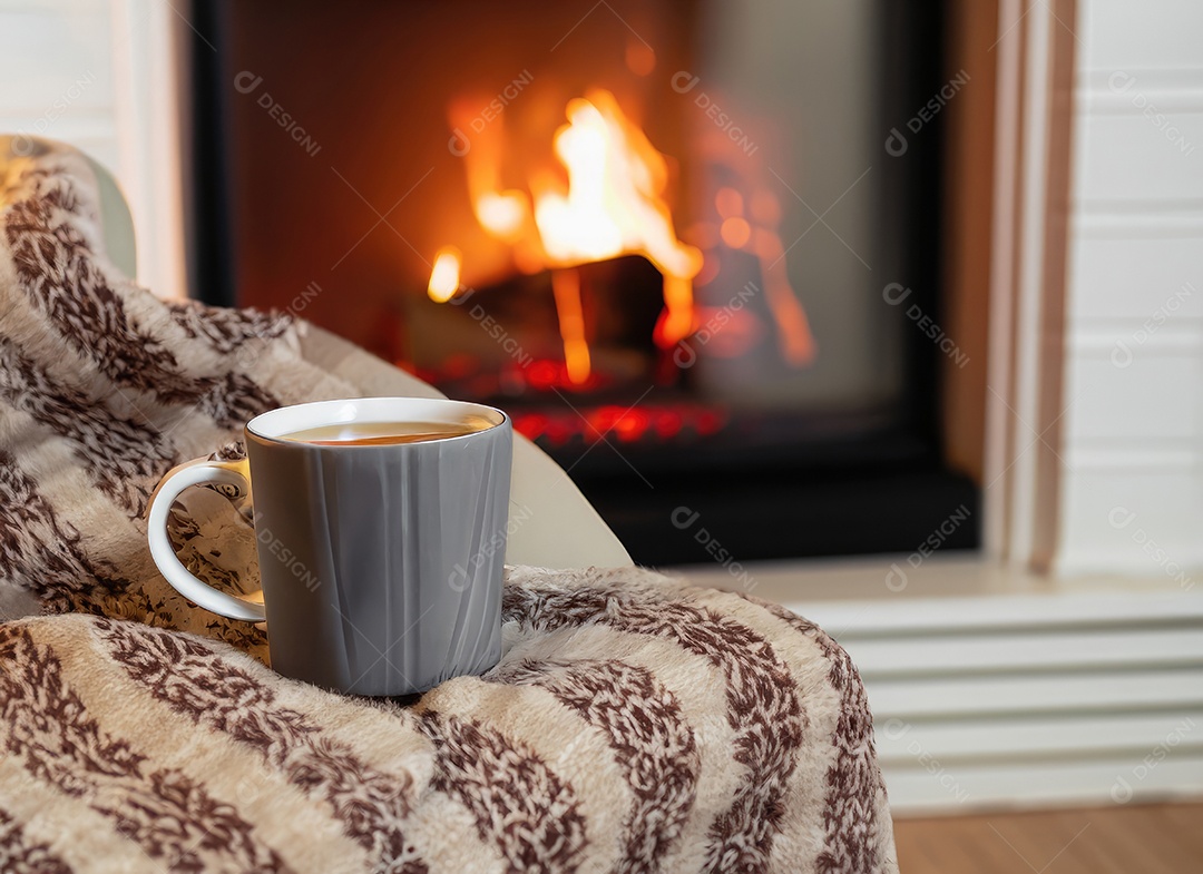 Uma caneca de chá quente está sobre uma cadeira com um cobertor de lã em um ambiente aconchegante