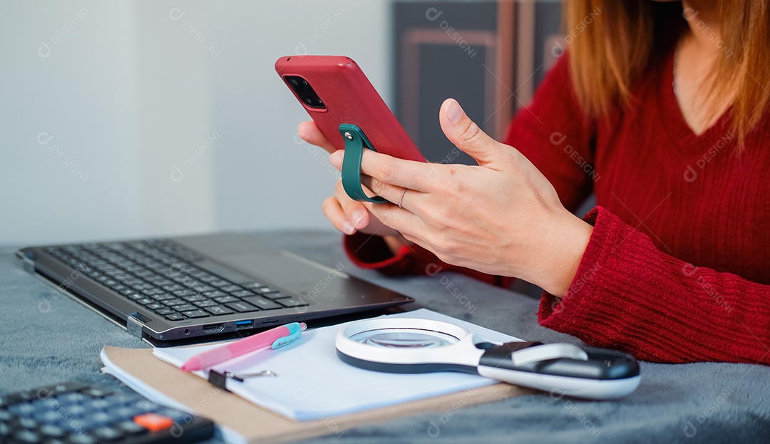 Uma mulher mexendo no celular e trabalhando no laptop