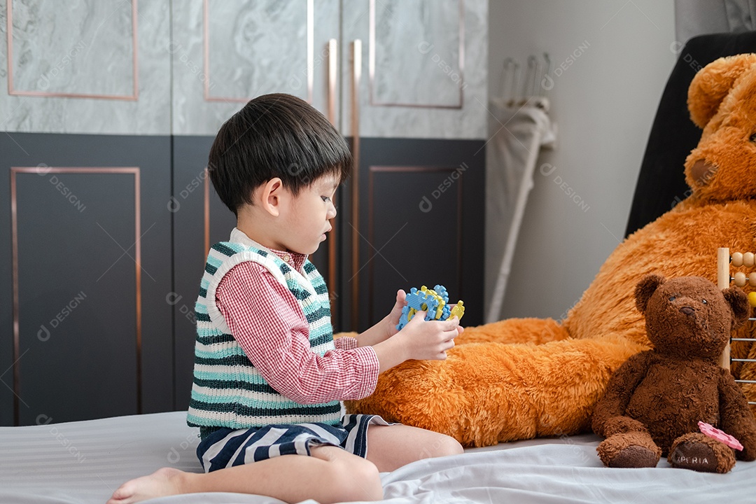 Menino asiático brincando com quebra-cabeças na cama alegremente