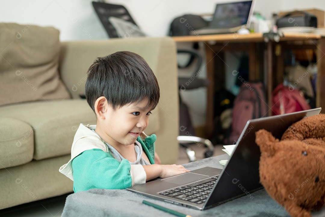 Um lindo menino asiático assistindo no laptop com seu urso de pelúcia