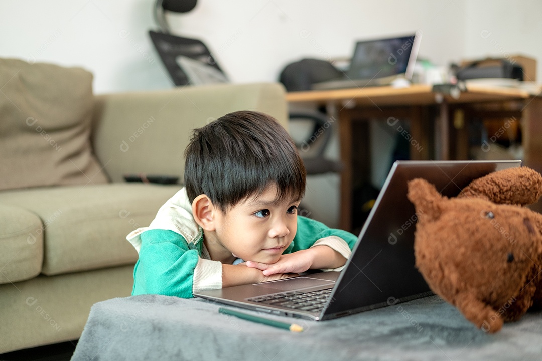 Um lindo menino asiático assistindo no laptop com seu urso de pelúcia