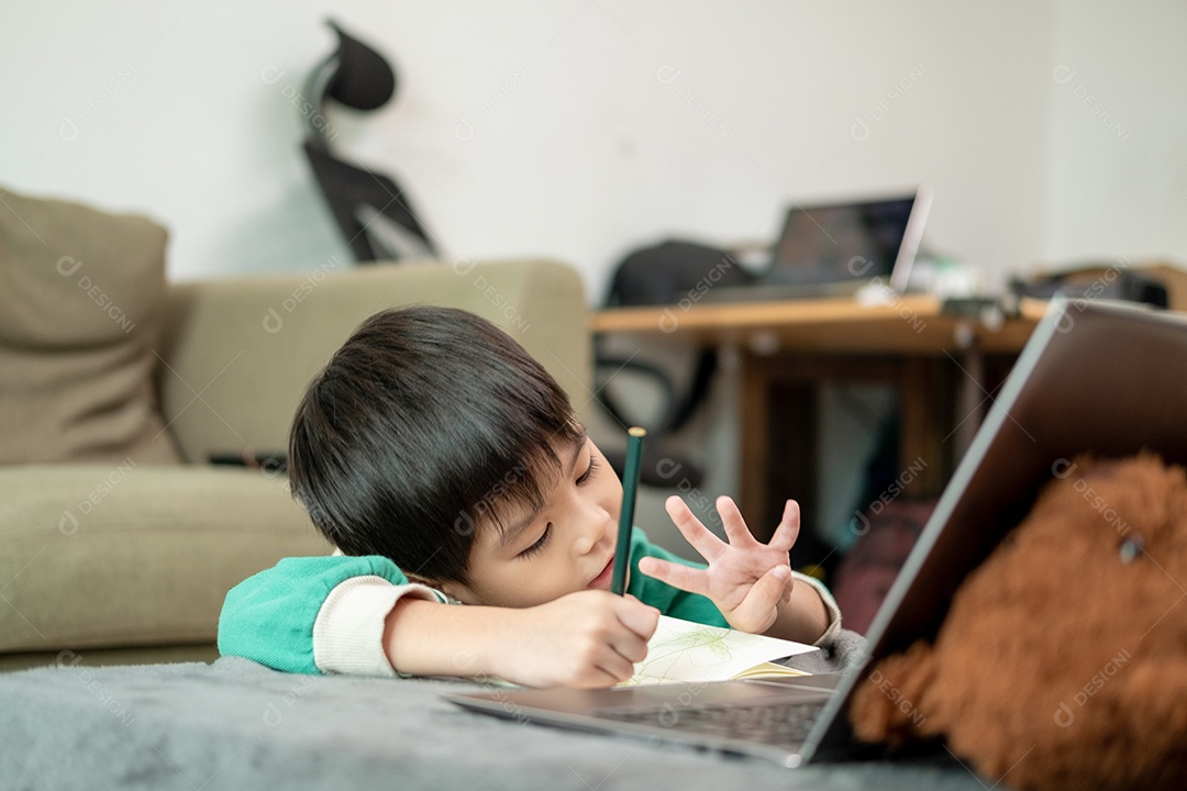 Um garotinho asiático desenhando e fazendo números na frente do laptop