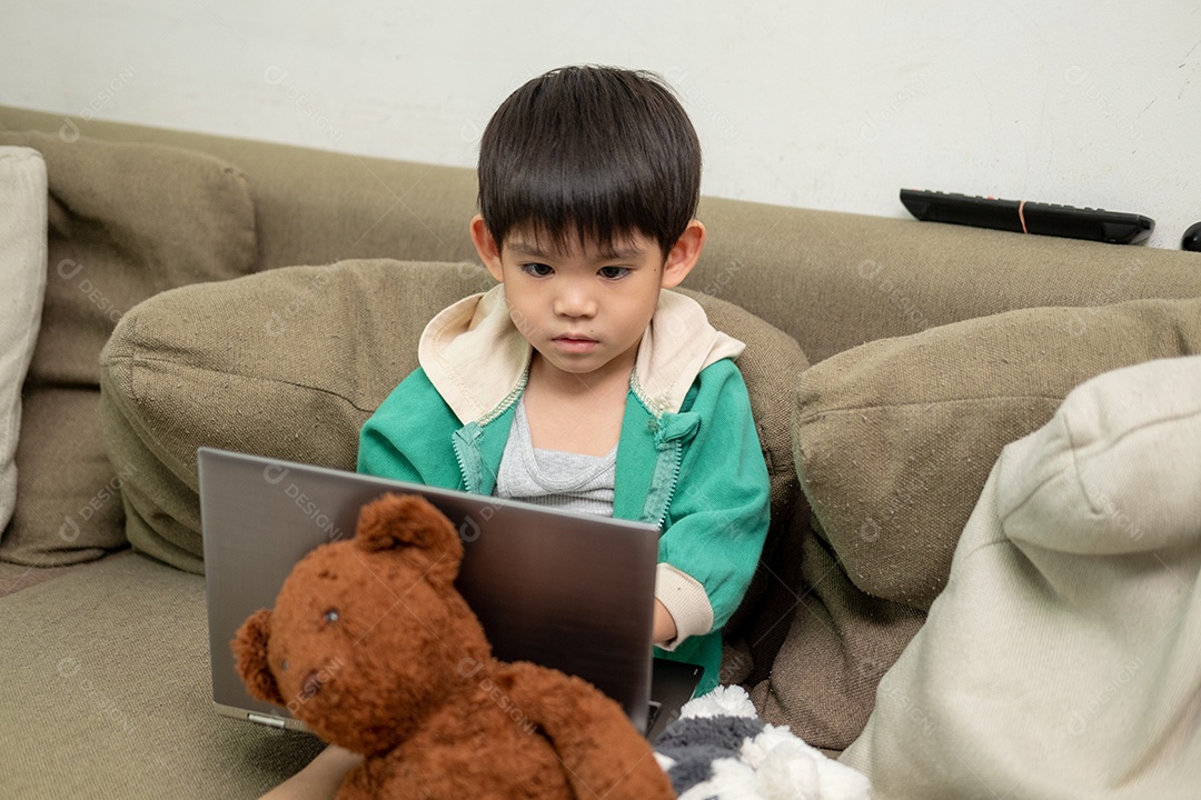 Um lindo menino asiático assistindo no laptop com seu urso de pelúcia