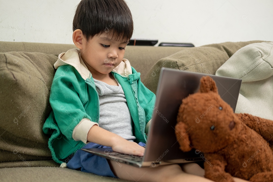 Um lindo menino asiático assistindo no laptop com seu urso de pelúcia