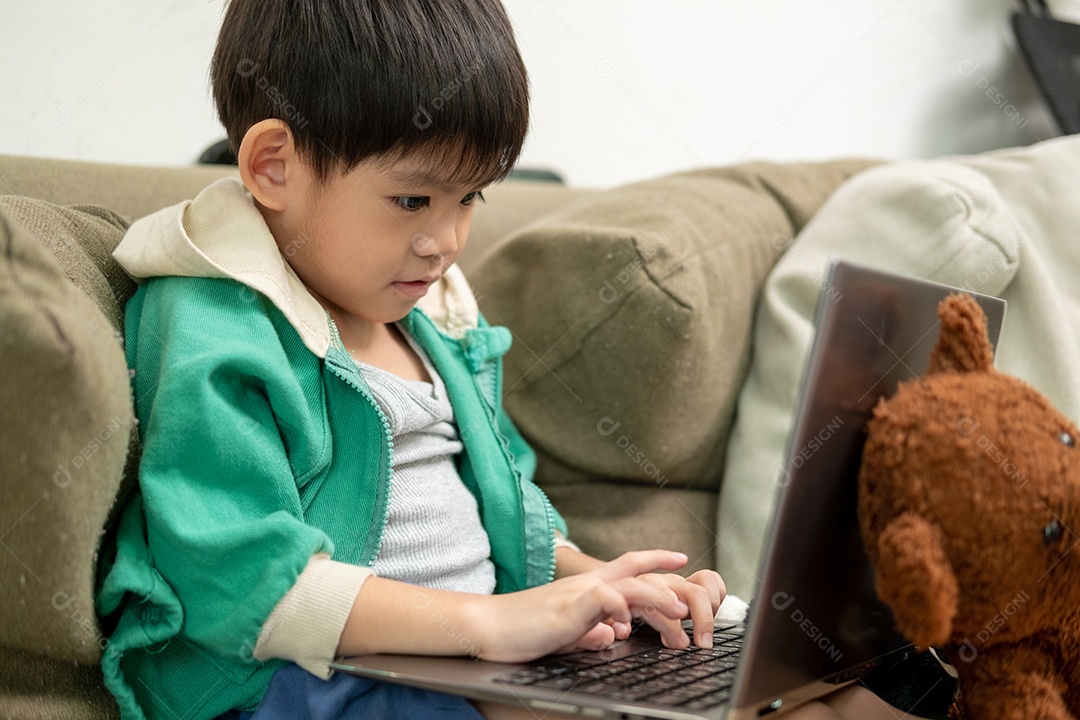 Um lindo menino asiático assistindo no laptop com seu urso de pelúcia