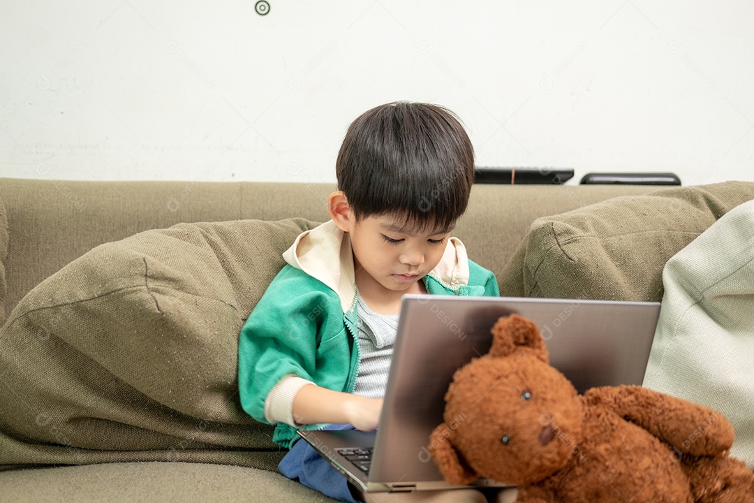 Um lindo menino asiático assistindo no laptop com seu urso de pelúcia