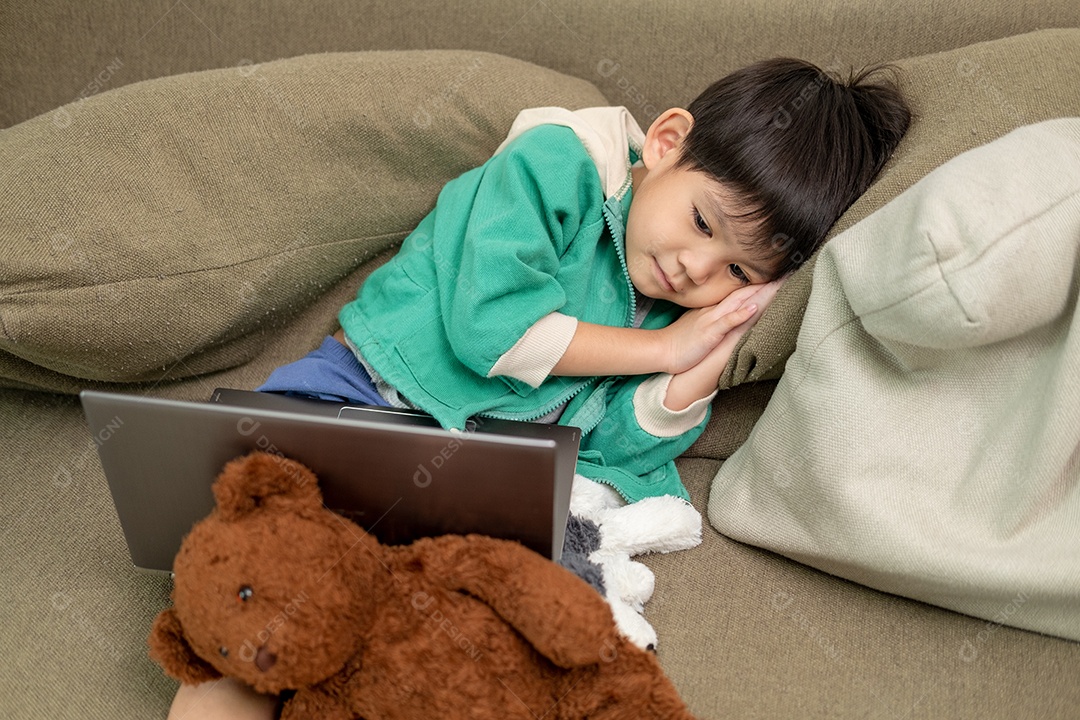 Um lindo menino asiático assistindo no laptop com seu urso de pelúcia