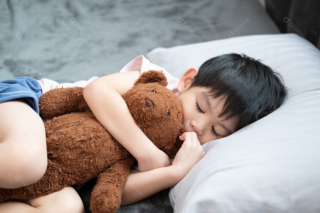 Um menino está dormindo e abraçando um ursinho de pelúcia na cama