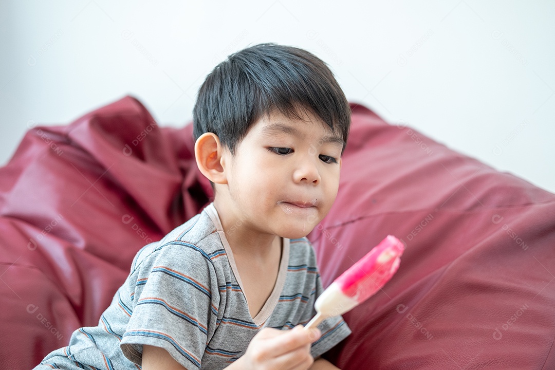 Um menino asiático está comendo um delicioso sorvete em uma cadeira