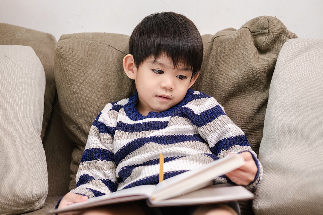 Menino asiático lendo um livro no sofá aprendendo fora da sala de aula