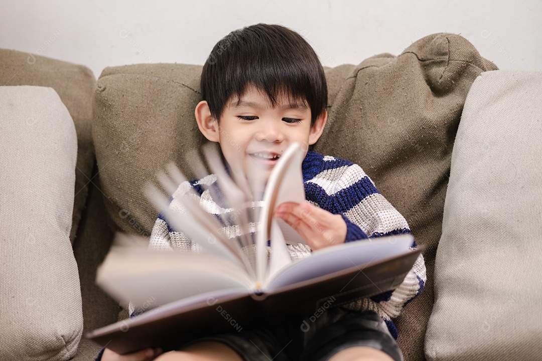 Menino asiático lendo um livro no sofá aprendendo fora da sala de aula