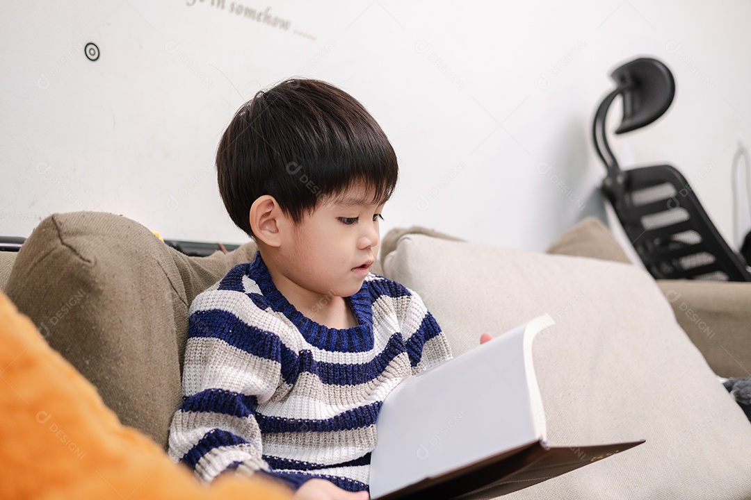 Menino asiático lendo um livro no sofá aprendendo fora da sala de aula