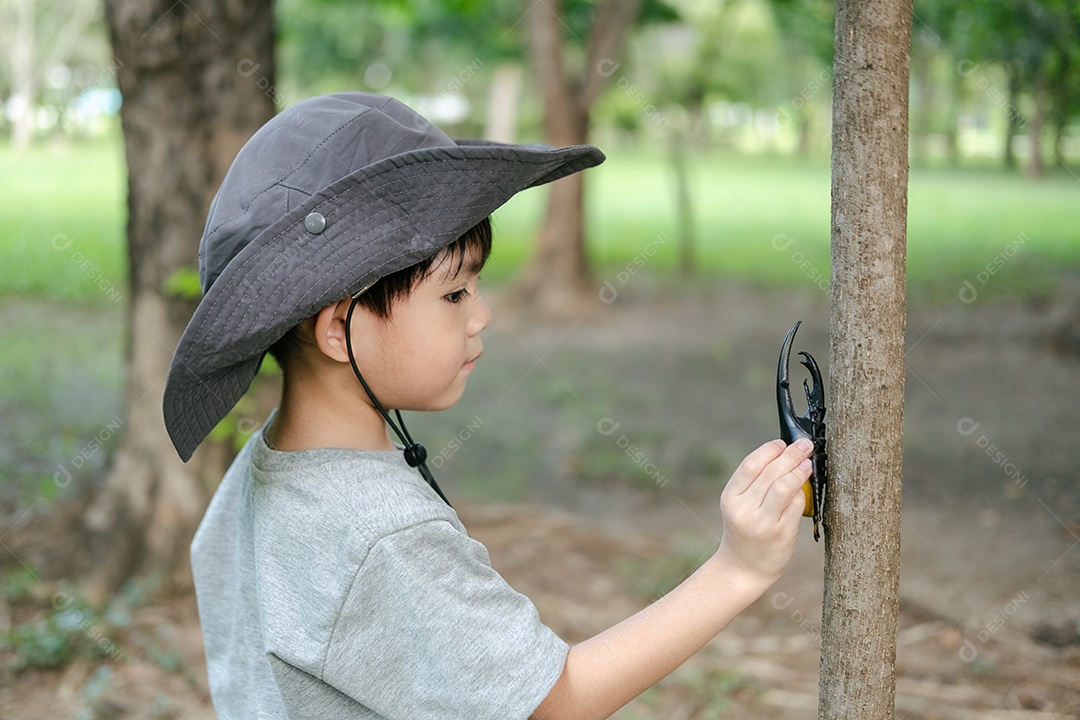 Menino asiático usando chapéu e traje de exploração florestal brinca com um besouro na mão