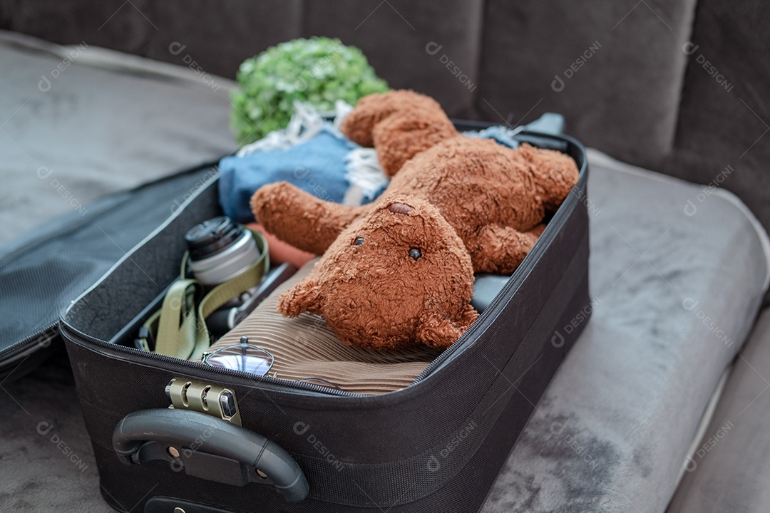 Conjunto de roupas e acessórios em uma mala com um urso de pelúcia
