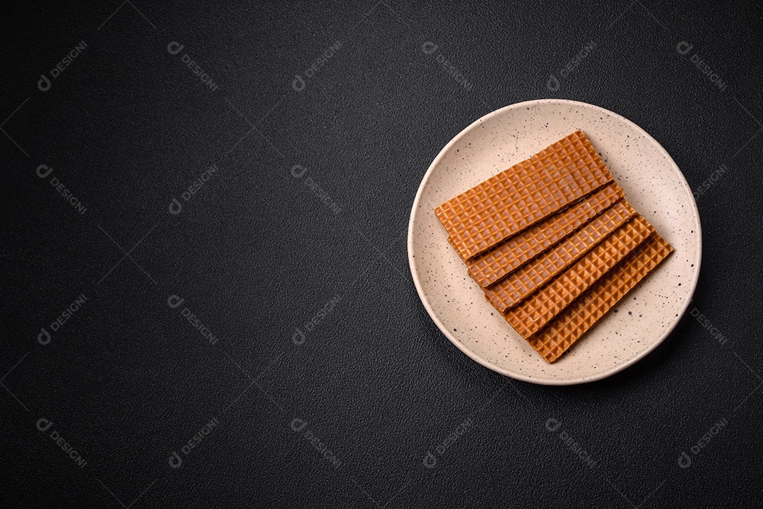 Deliciosos waffles retangulares crocantes e doces em uma placa de cerâmica sobre um fundo escuro de concreto