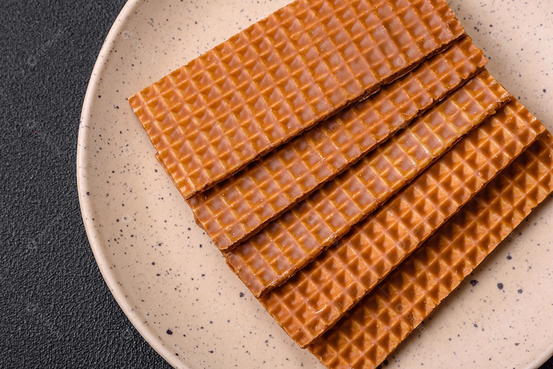 Deliciosos waffles retangulares crocantes e doces em uma placa de cerâmica sobre um fundo escuro de concreto