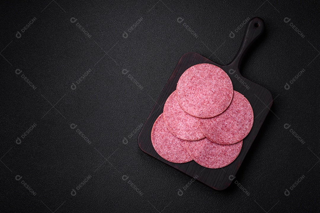 Deliciosa salsicha de salame fumado com sal, especiarias e ervas cortadas em fatias sobre um fundo escuro de concreto