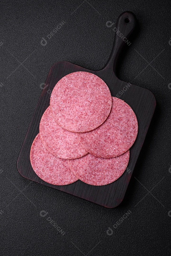 Deliciosa salsicha de salame fumado com sal, especiarias e ervas cortadas em fatias sobre um fundo escuro de concreto