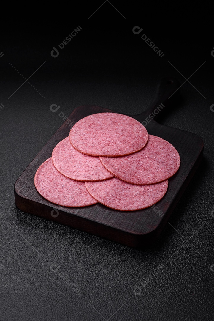 Deliciosa salsicha de salame fumado com sal, especiarias e ervas cortadas em fatias sobre um fundo escuro de concreto