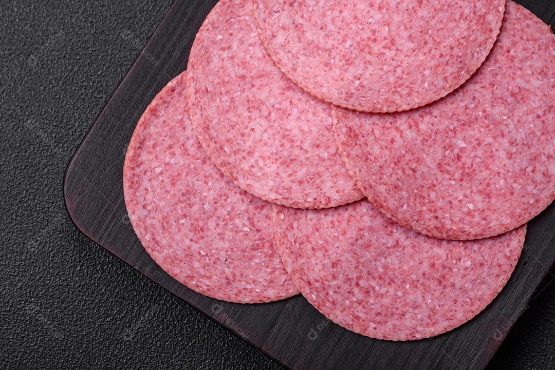 Deliciosa salsicha de salame fumado com sal, especiarias e ervas cortadas em fatias sobre um fundo escuro de concreto