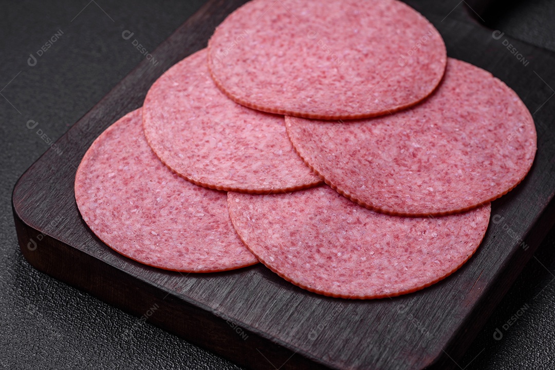 Deliciosa salsicha de salame fumado com sal, especiarias e ervas cortadas em fatias sobre um fundo escuro de concreto
