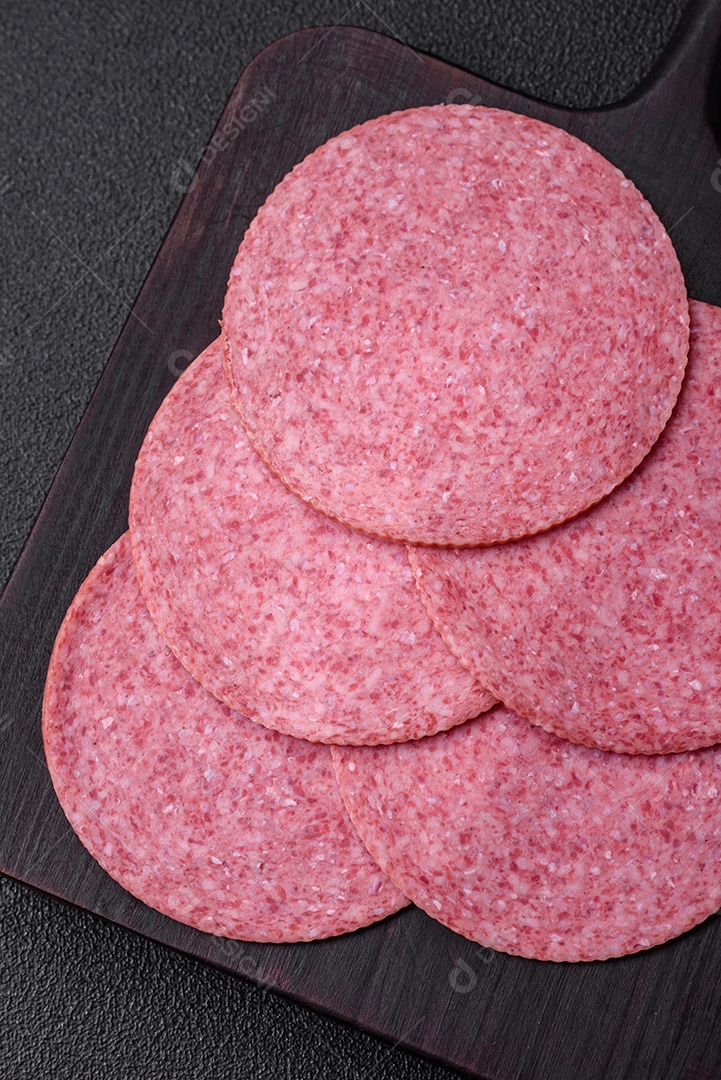 Deliciosa salsicha de salame fumado com sal, especiarias e ervas cortadas em fatias sobre um fundo escuro de concreto