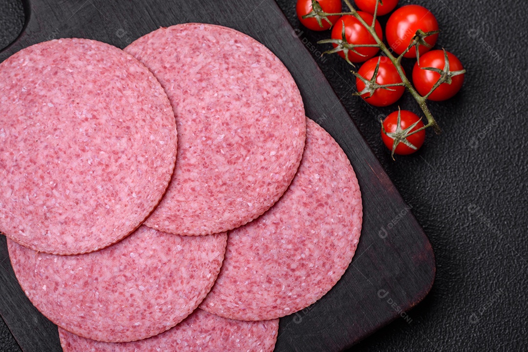 Deliciosa salsicha de salame fumado com sal, especiarias e ervas cortadas em fatias sobre um fundo escuro de concreto