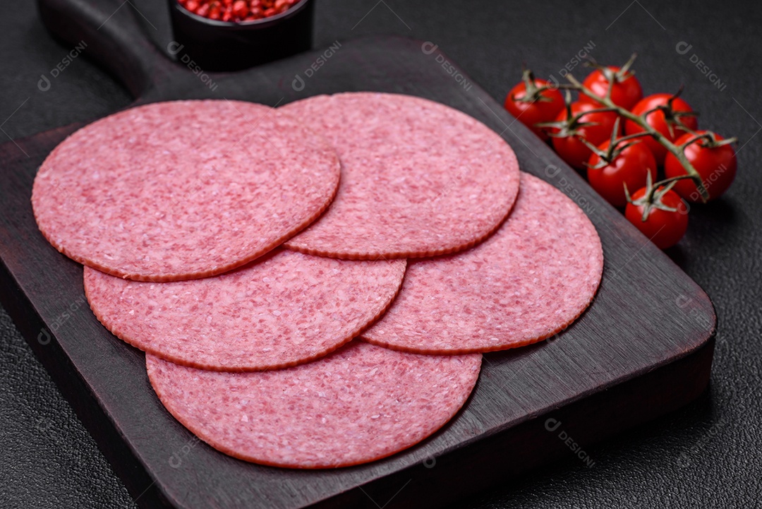 Deliciosa salsicha de salame fumado com sal, especiarias e ervas cortadas em fatias sobre um fundo escuro de concreto