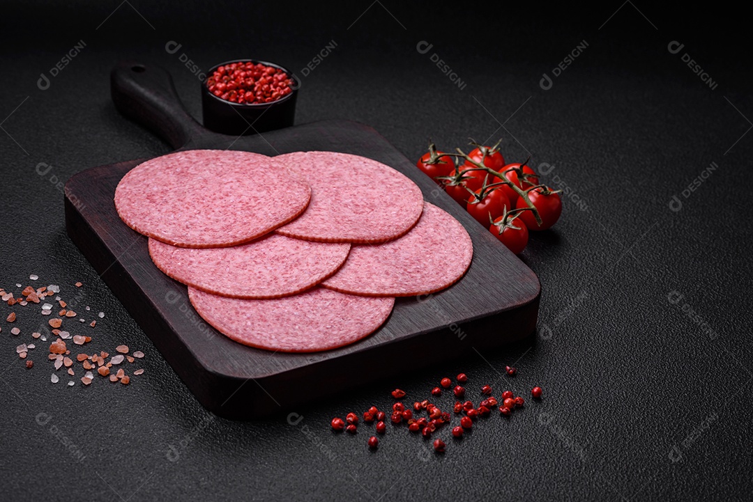 Deliciosa salsicha de salame fumado com sal, especiarias e ervas cortadas em fatias sobre um fundo escuro de concreto