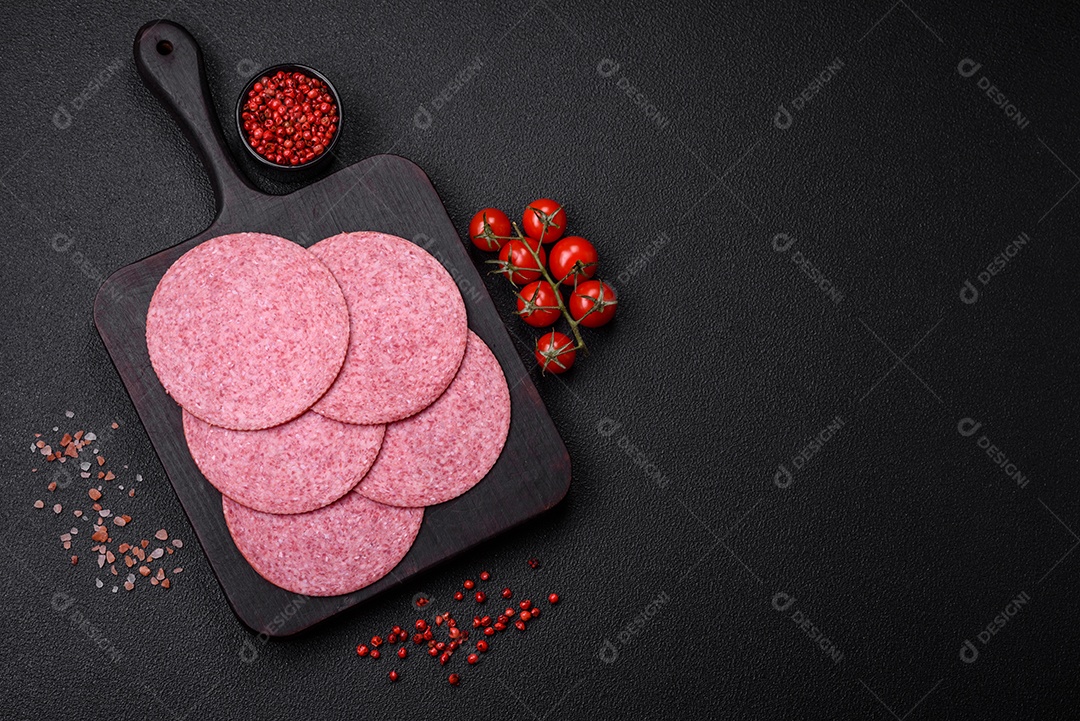 Deliciosa salsicha de salame fumado com sal, especiarias e ervas cortadas em fatias sobre um fundo escuro de concreto