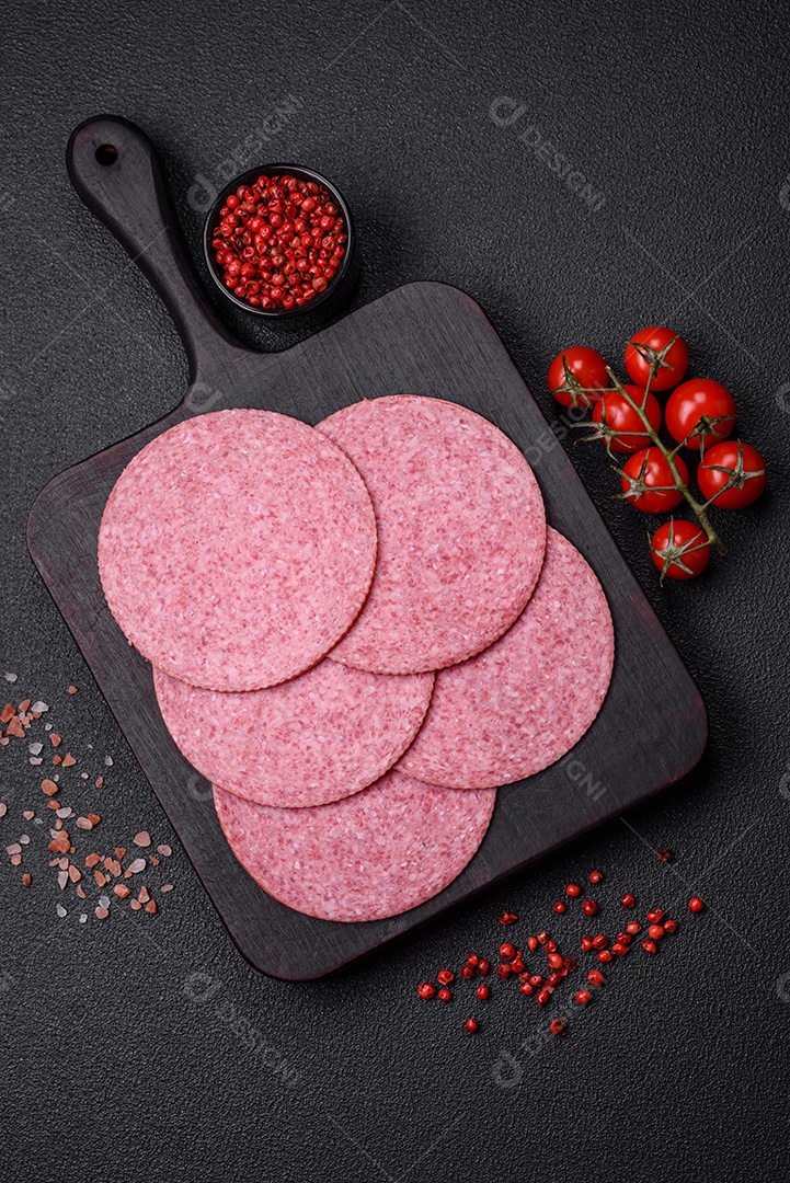 Deliciosa salsicha de salame fumado com sal, especiarias e ervas cortadas em fatias sobre um fundo escuro de concreto