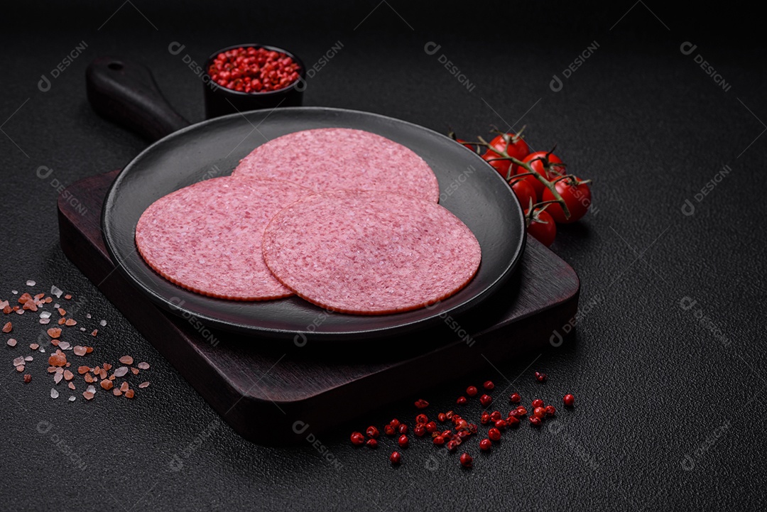 Deliciosa salsicha de salame fumado com sal, especiarias e ervas cortadas em fatias sobre um fundo escuro de concreto