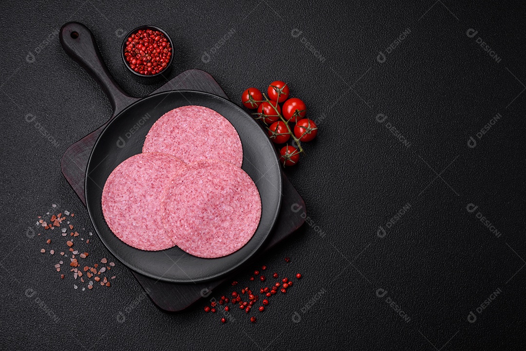 Deliciosa salsicha de salame fumado com sal, especiarias e ervas cortadas em fatias sobre um fundo escuro de concreto