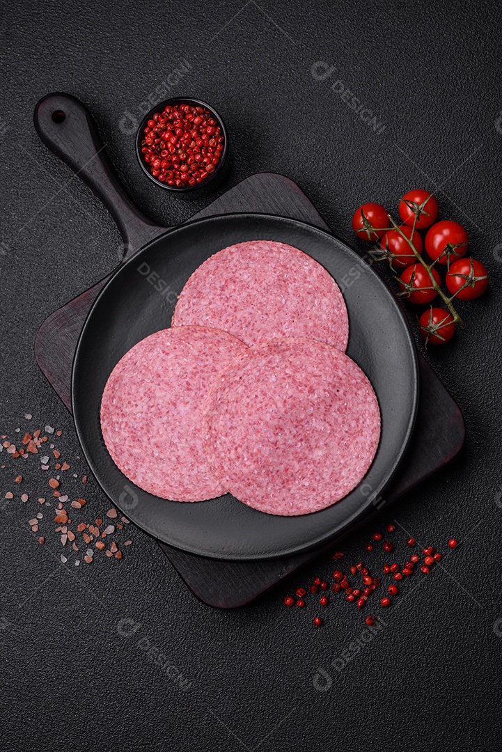 Deliciosa salsicha de salame fumado com sal, especiarias e ervas cortadas em fatias sobre um fundo escuro de concreto