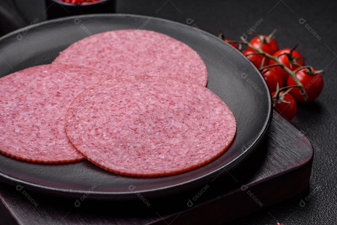 Deliciosa salsicha de salame fumado com sal, especiarias e ervas cortadas em fatias sobre um fundo escuro de concreto