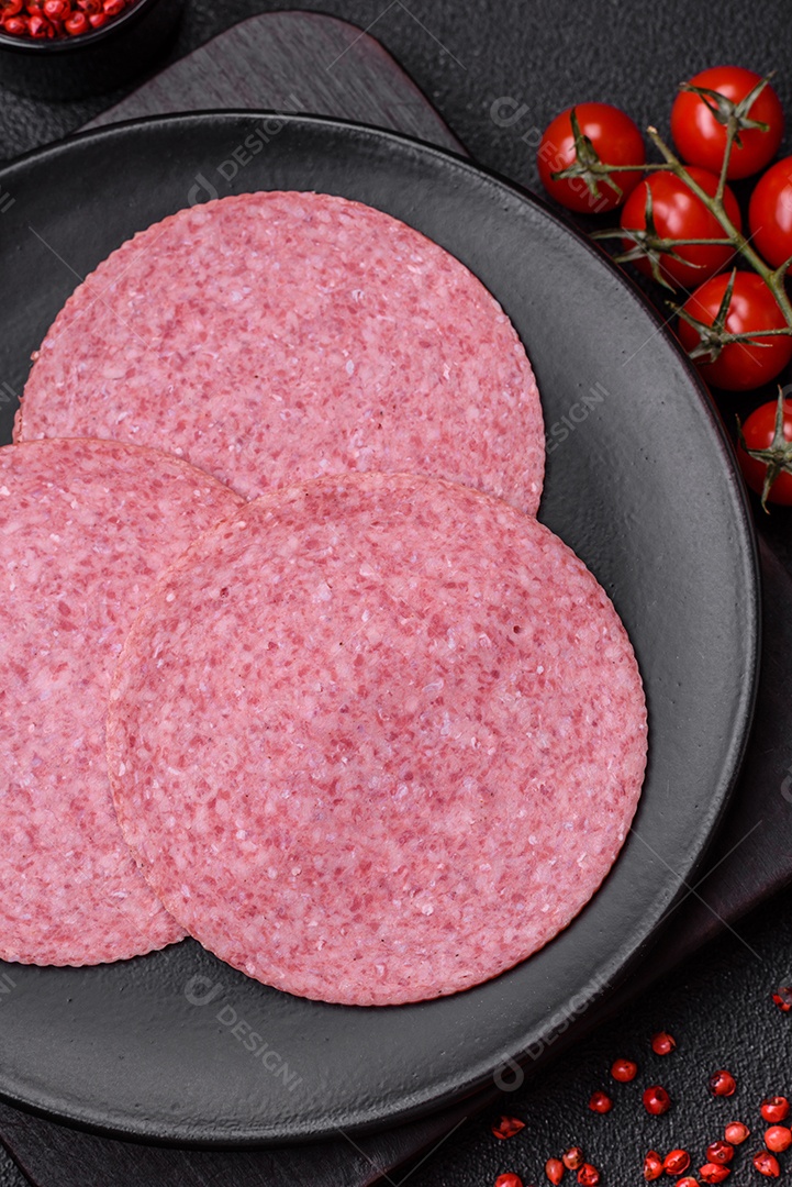 Deliciosa salsicha de salame fumado com sal, especiarias e ervas cortadas em fatias sobre um fundo escuro de concreto