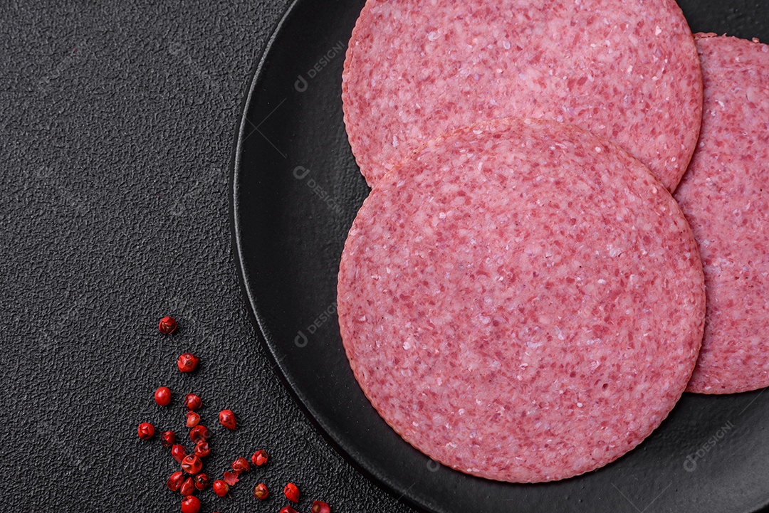 Deliciosa salsicha de salame fumado com sal, especiarias e ervas cortadas em fatias sobre um fundo escuro de concreto