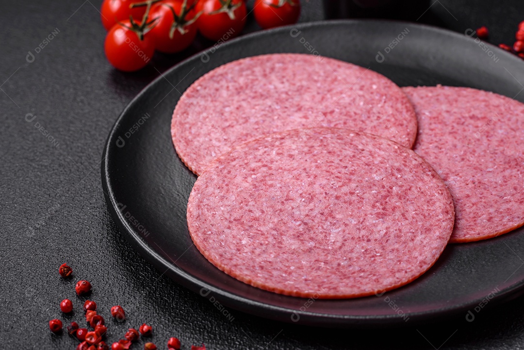 Deliciosa salsicha de salame fumado com sal, especiarias e ervas cortadas em fatias sobre um fundo escuro de concreto