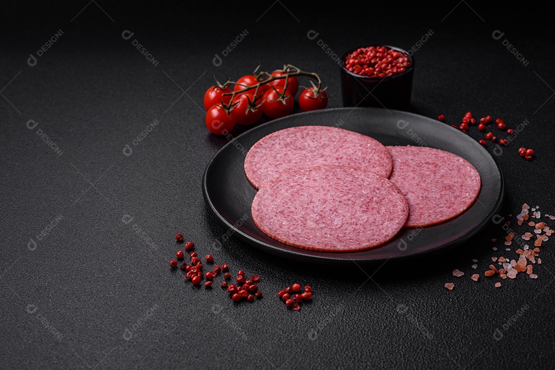 Deliciosa salsicha de salame fumado com sal, especiarias e ervas cortadas em fatias sobre um fundo escuro de concreto