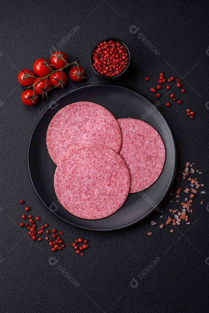 Deliciosa salsicha de salame fumado com sal, especiarias e ervas cortadas em fatias sobre um fundo escuro de concreto