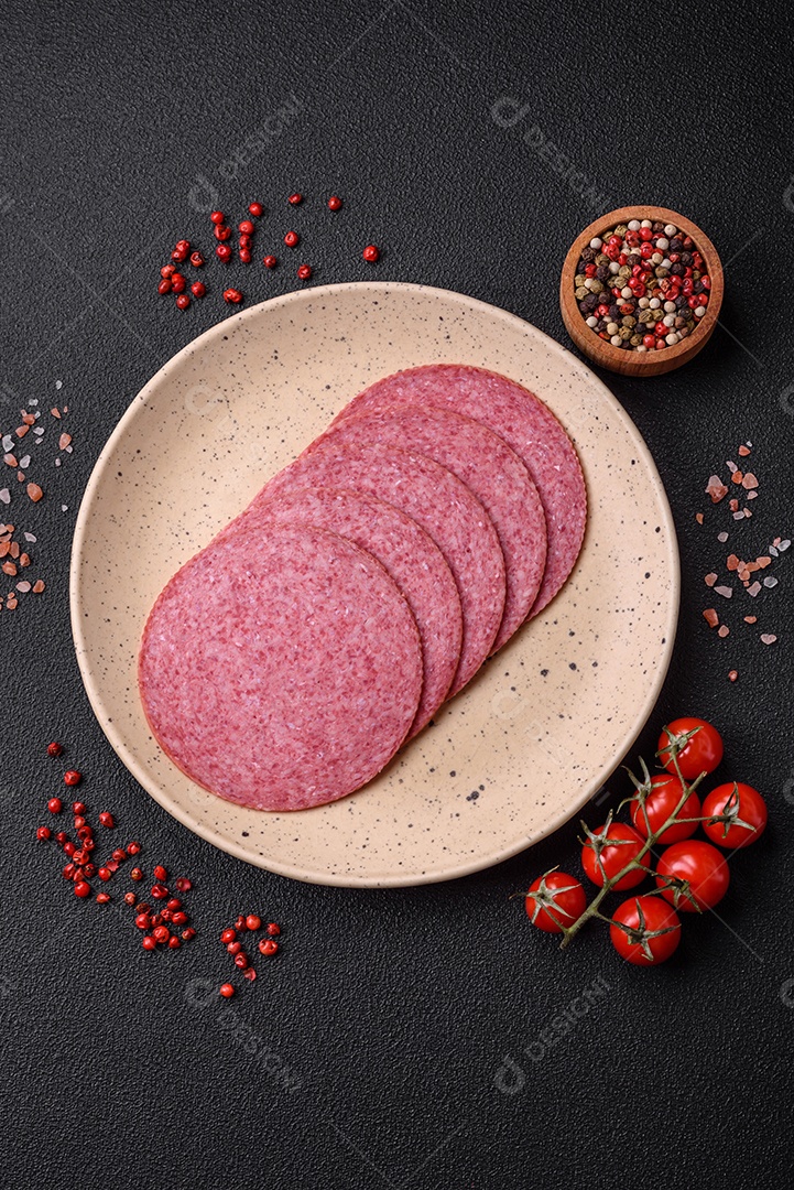 Deliciosa salsicha de salame fumado com sal, especiarias e ervas cortadas em fatias sobre um fundo escuro de concreto