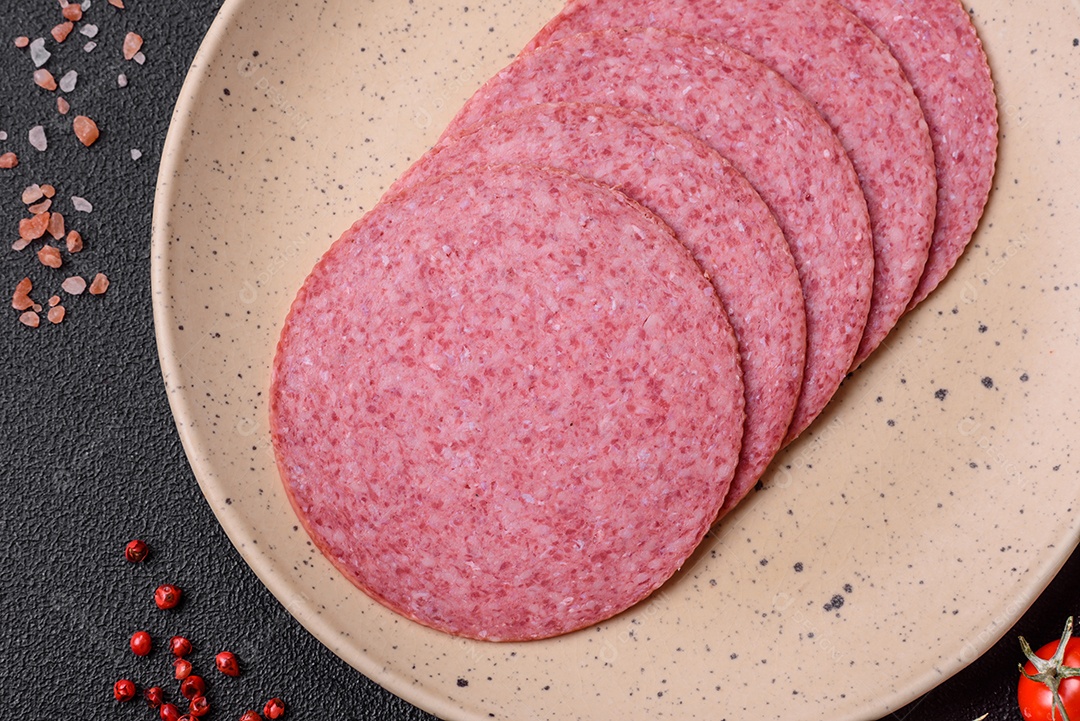 Deliciosa salsicha de salame fumado com sal, especiarias e ervas cortadas em fatias sobre um fundo escuro de concreto